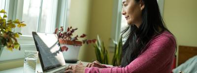 Asian woman using her laptop at her desk by a window