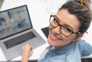 Female marketing professional working on laptop and smiling at the camera