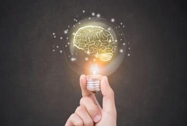 Hand holding a lightbulb featuring a lit up brain within