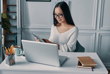 Woman sitting in front of laptop in home office, looking at smartphone