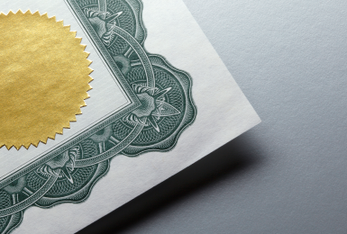 A gold seal on an award certificate resting on a gray background. The certificate is slightly lifted off of the surface.