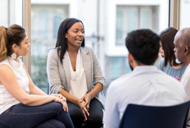 Group of adults sitting in a circle with one young woman leading the discussion