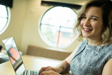 Female online student smiling at camera while typing on laptop