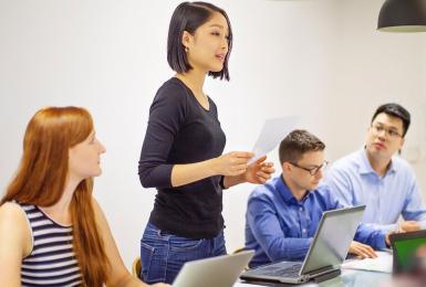 Female employee standing at meeting room table presenting a document