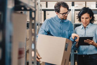 Two supply chain management professionals looking at tablet and walking through warehouse