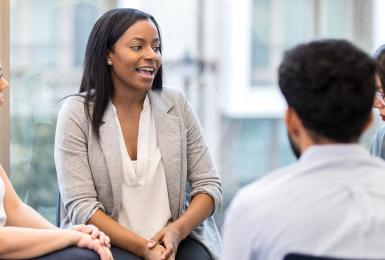 Group of adults sitting in a circle with one young woman leading the discussion