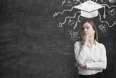 Woman standing in front of blackboard with chalk drawing of graduation cap above her head