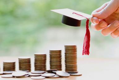 Stacks of quarters lined up, increasing as they go with miniture graduation cap at the top 