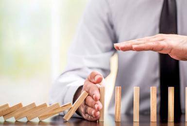 Dominoes falling over with a professionals hand blocking the rest from falling 