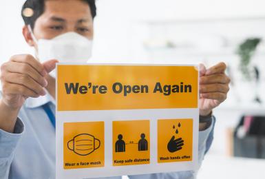 Asian businessman wear face mask attach reopen sign at office after lockdown due to coronavirus covid-19, business new normal and social distancing concept.