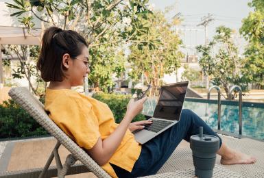 Young asian businesswoman using smart phone and typing on laptop computer for sharing social media sitting in bed at outdoor.