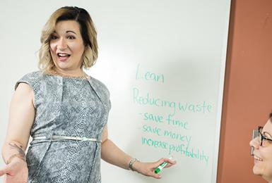 Blond woman at white board speaking to two other women, 