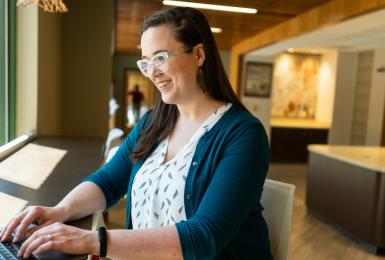 Woman sits in cafe window working on laptop