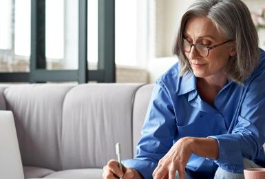 Mature woman studying on laptop and writing in notebook