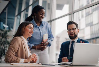 Three business professionals collaborating around a laptop in a bright, modern office