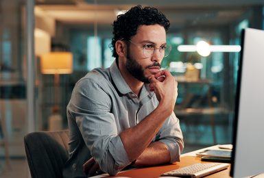 A young professional man with glasses sits at a desk in a modern office