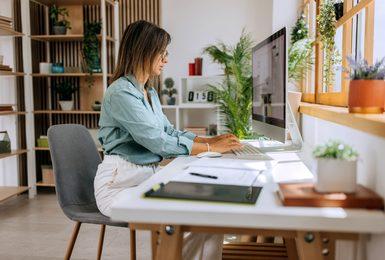 Woman working at a desktop computer at a home office desk, reviewing a digital marketing campaign