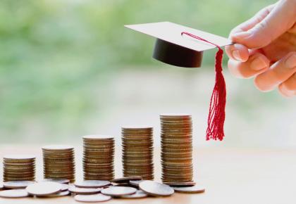 Stacks of quarters lined up, increasing as they go with miniture graduation cap at the top