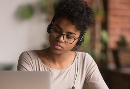 Female millennial online student wearing headphones and looking at laptop