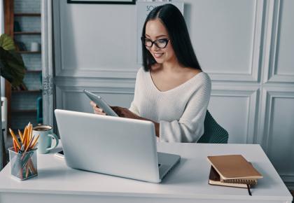 Woman sitting in front of laptop in home office, looking at smartphone