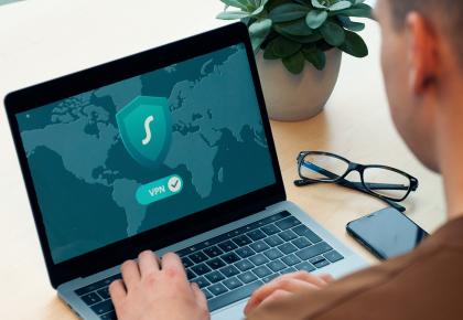 Man sits in front of laptop, which displays shield and VPN symbol