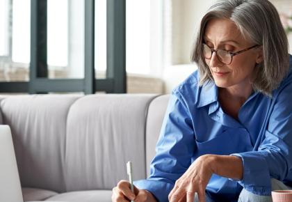 Mature woman studying on laptop and writing in notebook