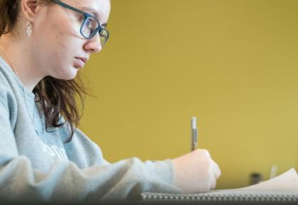 Female student sitting at a desk while taking notes.