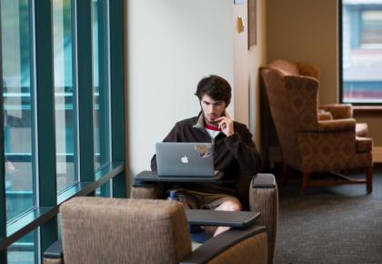 Teen male student studying at desk with open latop