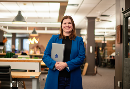 Woman standing in library holding laptop smiling portrait