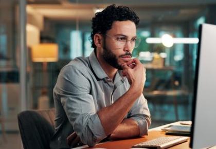 A young professional man with glasses sits at a desk in a modern office