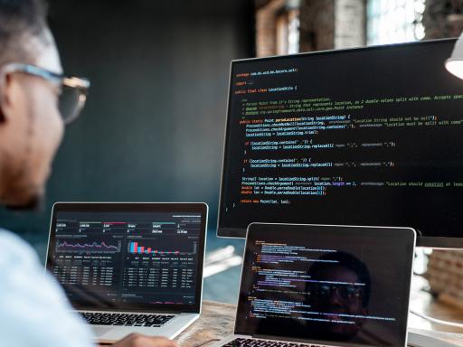 Man looking at three computer screens with code on them