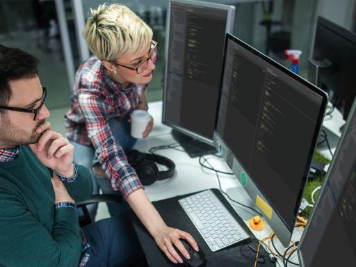 Two coworkers look at code on a computer screen