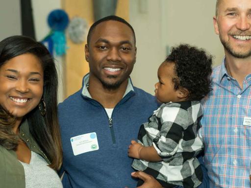 Adult male students at graduation party with his family and a staff member smiling at the camera