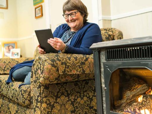 Female student working on tablet next to her fireplace while sitting on her couch