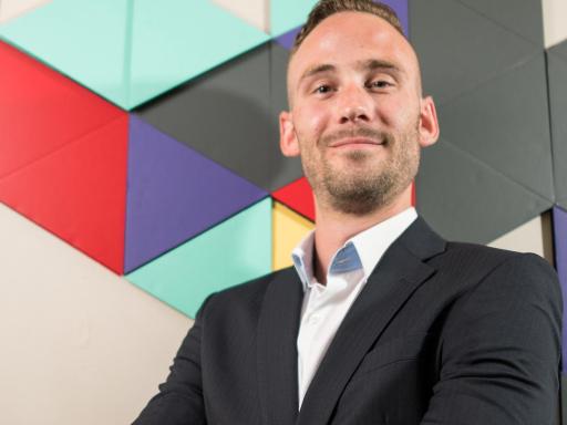 Adult male student in front of colorful geometric office artwork smiling at camera