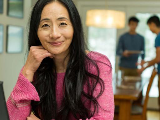 Asian woman at laptop with family in background