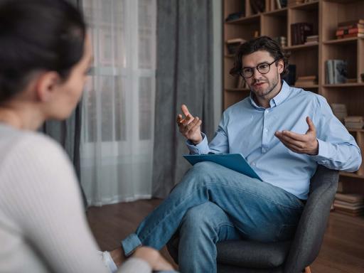 Male counselor in chair with clipboard and female patient talking with him