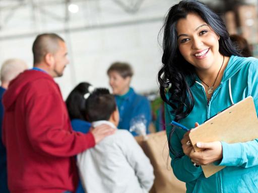 Dark haired woman with clipboard and a group of people talking behind her