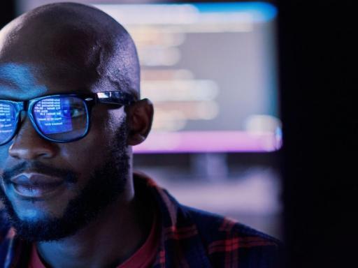 african american man with glasses facing a monitor with the glare reflecting on his glasses