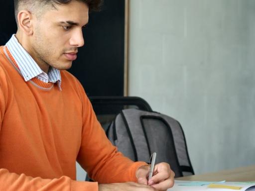 male in orange sweater at table with laptop