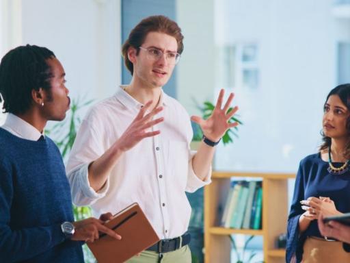 Group of five young professionals with man in the center speaking to the rest who are looking at him