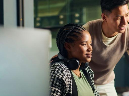 woman sitting and a man standing to her left both looking at two monitors