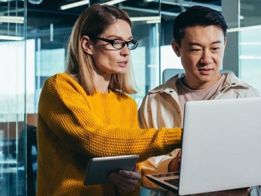 woman in yellow shirt pointing at laptop talking to asian man