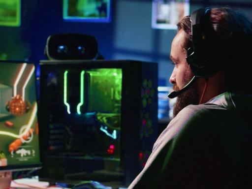 Male gamer facing his monitor with headset on in a dark room with other monitors lit up