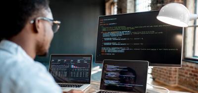 C++ Programmer working on code in front of multiple computer monitors in office setting