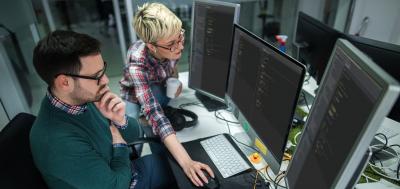 Two coworkers look at code on a computer screen