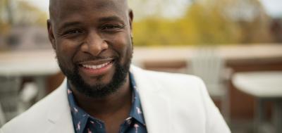 Black man well-dressed and standing on balcony smiling