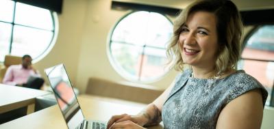 Female online student smiling at camera while typing on laptop