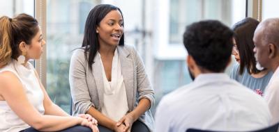 Group of adults sitting in a circle with one young woman leading the discussion