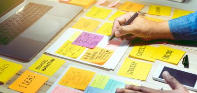 Image of person holding pen over multi-colored sticky notes on a desk